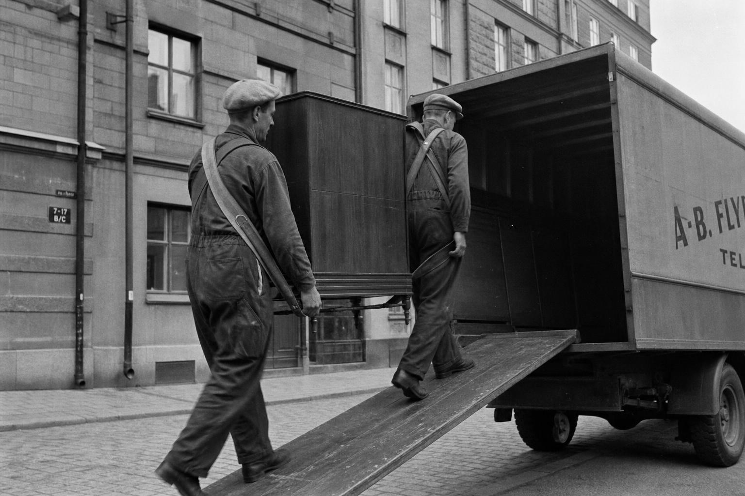 Flyttgubbar lastar en flyttbil från 1950-talet på en kullerstensgata i Stockholm